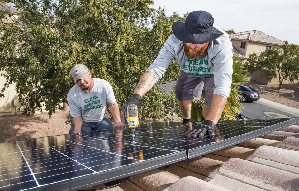 Larry Chambers (left) and Chris Miller, solar panel installers for SunHarvest Solar, install panels on a home in El Mirage on Nov. 20, 2018.