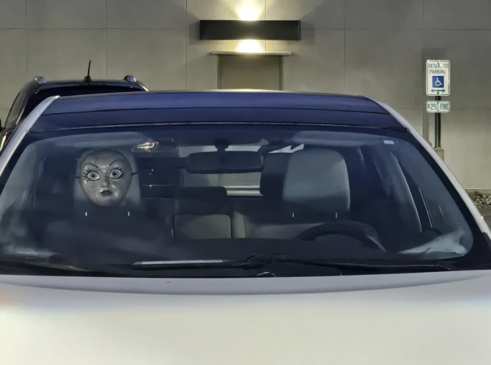 Reflective mask on car's dashboard gives illusion of face peeking out from behind windshield