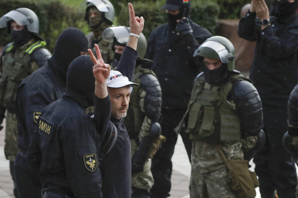 A man makes v-signs in front of a riot police blockade as he is detained during a protest at the Independence Square in Minsk, Belarus, Thursday, Aug. 27, 2020. Police in Belarus have dispersed protesters who gathered on the capital's central square, detaining dozens. (AP Photo/Sergei Grits)