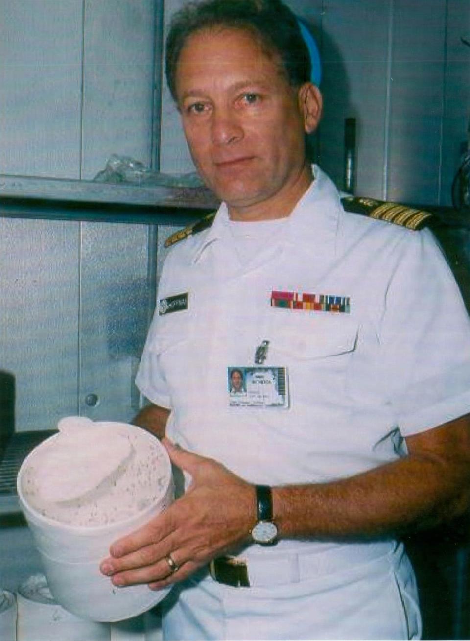 man in navy uniform, holding malaria mosquitos in container