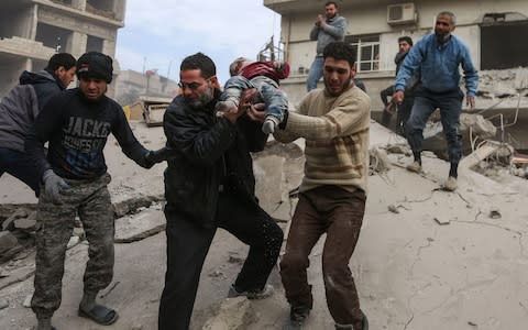 A man hands over a child to his father after being rescued from beneath the ruins of a building that collapsed following air strikes in besieged Eastern Ghouta - Credit: AFP