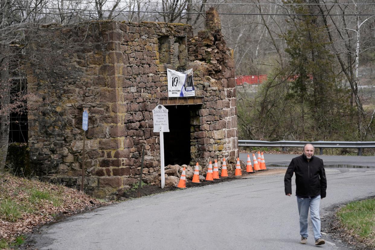 man walks up road past crumbling brick structure with rocks in the entrance and traffic cones blocking it off