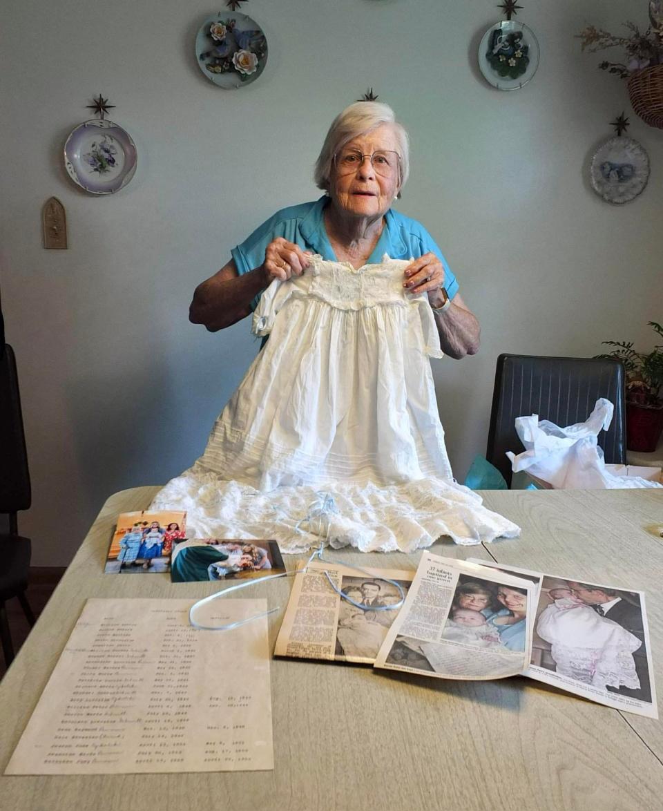 Bernadine (Bernie) Knier of Greendale holds up the baptismal dress her family has been using since 1905 with various articles, photos and records about its history on the table. The dress has been worn by 40 people for their baptisms.