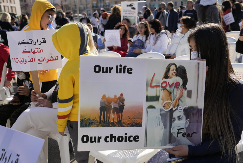 Protesters hold placards during a rally to protest measures imposed against people who are not vaccinated, in Beirut, Lebanon, Saturday, Jan. 8, 2022. Vaccination is not compulsory in Lebanon but in recent days authorities have become more strict in dealing with people who are not inoculated or don't carry a negative PCR test. They Arabic placard, left, reads:"Your decisions is a violation of international law." (AP Photo/Hussein Malla)