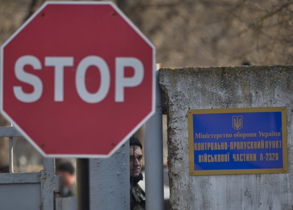 FILE - In this Wednesday, March 12, 2014 file photo, a Ukrainian soldier peers from behind the gate of the Ukrainian infantry base in Perevalne, Ukraine. On the eve of a referendum vote that has the Black Sea peninsula resting on a razor’s edge, those facing the greatest and most fraught uncertainty was are Ukraine’s military forces on the peninsula, who have been hemmed in by heavily armed Russian troops and warned by the region’s pro-Russian leader that they would be considered “illegal” if they didn’t surrender. (AP Photo/Vadim Ghirda, File)