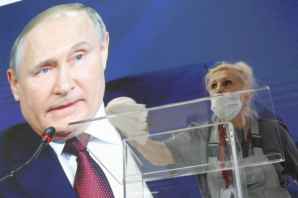 A worker cleans a speaker's podium as Russian President Vladimir Putin seen on a screen in the background at the St. Petersburg International Economic Forum in St. Petersburg, Russia, Friday, June 4, 2021. Russian President Vladimir Putin on Friday praised his country's response to the COVID-19 pandemic and called for a stronger global response to global warming. (AP Photo/Dmitri Lovetsky)