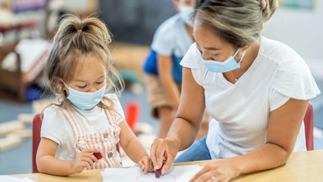 Cute young girl colouring in a daycare facility while wearing a protective face mask to avoid the transfer of germs during COVID-19.