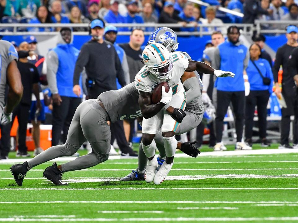 Tyreek Hill makes a catch while being tackled by two Lions defenders.