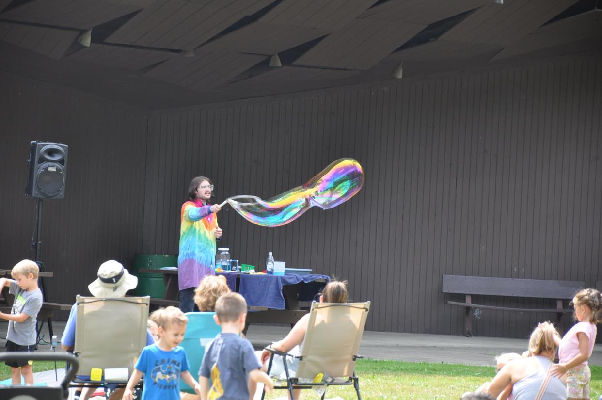 Kyle Rickert, a specialist at the Great Lakes Science Center in Cleveland, makes a huge wavy bubble with a large wand on Thursday, July 18, 2024, in Silver Park in Alliance. It was part of a free "Bubblemania" event there.