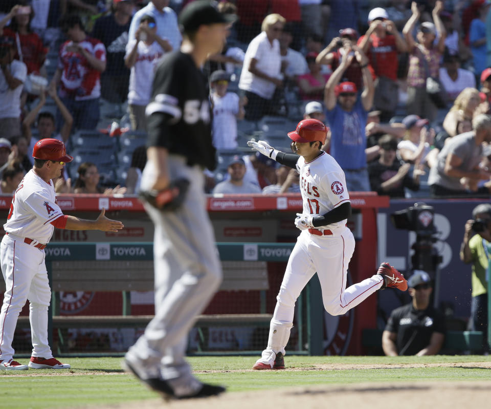 Los Angeles Angels third base coach Mike Gallego, back left, reaches to congratulate designated hitter Shohei Ohtani, right, who hit a two-run home run off Chicago White Sox's Ross Detwiler, center, during the seventh inning of a baseball game in Anaheim, Calif., Sunday, Aug. 18, 2019. (AP Photo/Alex Gallardo)