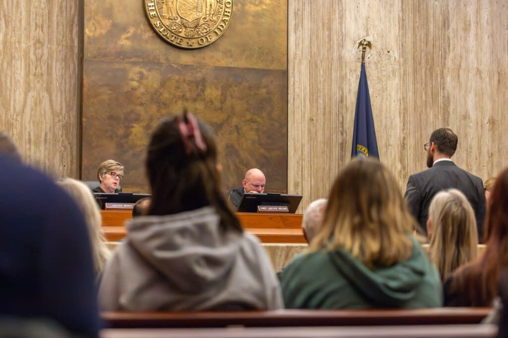 Two Idaho Supreme Court justices, in robes, listen to arguments in a packed courtroom