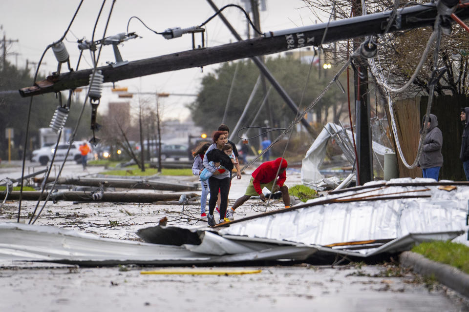 People cross under downed power lines where a tornado was reported to pass along Mickey Gilley Boulevard near Fairmont Parkway, Tuesday, Jan. 24, 2023, in Pasadena, Texas. (Mark Mulligan/Houston Chronicle via AP)