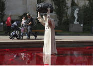 Visitors to the National Museum walk past a new statue of the late pope, St. John Paul II, throwing a stone at a "Poisoned Well" just hours before its official inauguration in the museum yard in Warsaw, Poland, Thursday, Sept. 24, 2020. The sculpture by Poland's Jerzy Kalina is said to be a response to a controversial 1999 sculpture by Italian Maurizio Cattelan in which the Polish-born pontiff was shown as being crushed by a similar stone. (AP Photo/Czarek Sokolowski)