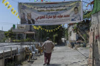 A Palestinian man passes under a banner with picture and name of slain Mohammed al-Alami, 12 and reads "Palestinian National Liberation movement, Fatah, offers her hero martyr child," infant of the family house, in the West Bank village of Beit Ummar, near Hebron, Wednesday, Aug. 4, 2021. (AP Photo/Nasser Nasser)