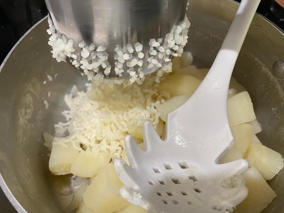 ricing mashed potatoes into a big metal pot
