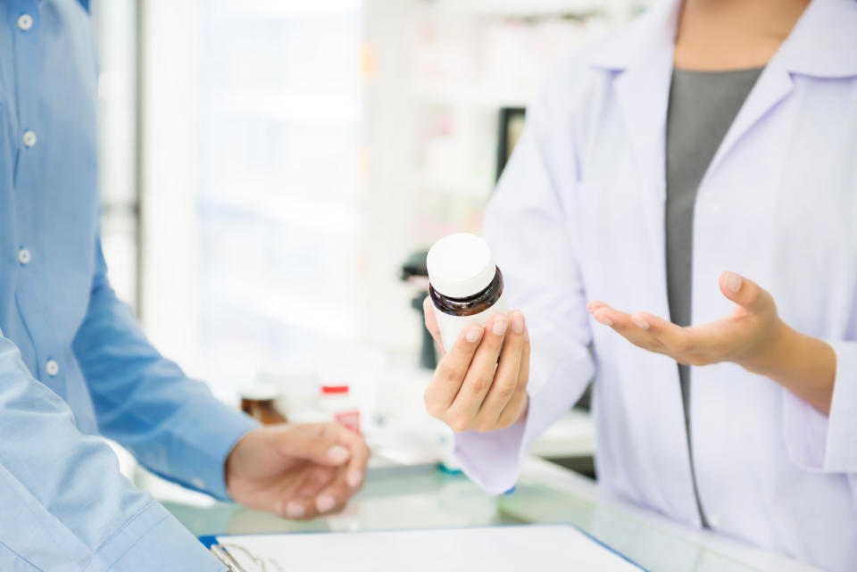 Female pharmacist holding medicine bottle giving advice to customer in chemist shop or pharmacy