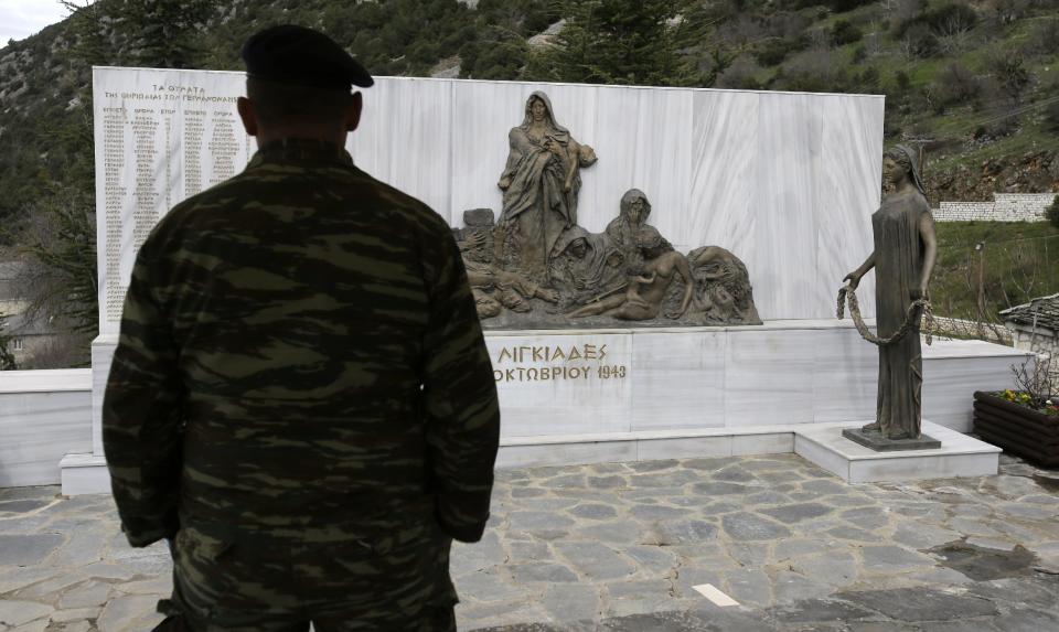 An army officer looks at the monument with the names of villagers who German army troops massacred, in the village of Ligiades near the northwestern town of Ioannina, Greece, on Thursday, March 6, 2014. German President Joachim Gauck's three-day visit to the country will include a speech Friday at the site where German army troops massacred 92 villagers near the northeastern town of Ioannina, and a meeting with the town's Jewish community. (AP Photo/Thanassis Stavrakis)