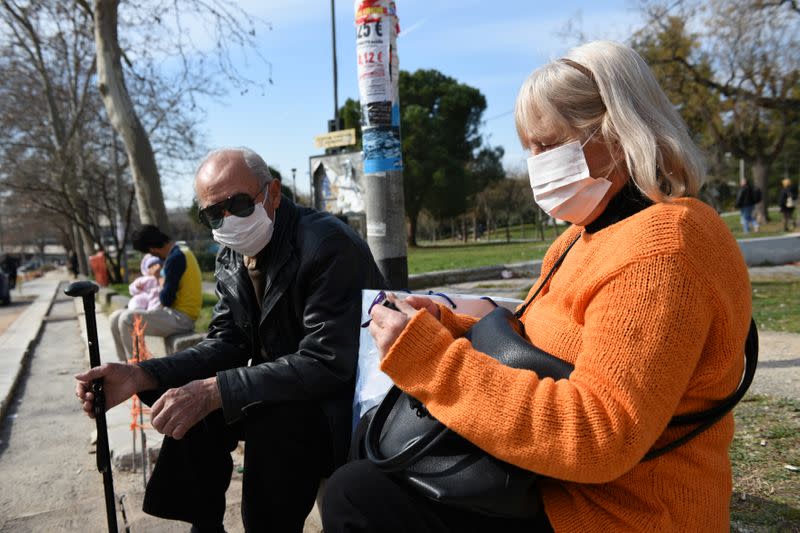 People wearing protective face masks sit outside the AHEPA hospital, where the first confirmed coronavirus case is being treated, in Thessaloniki