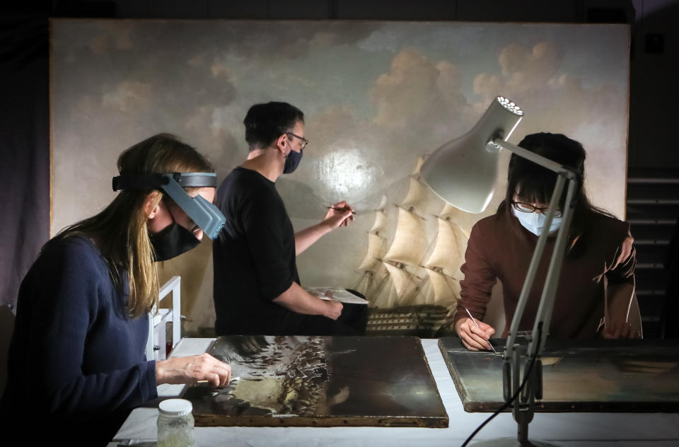 <p>Accredited Paintings Conservator Rhiannon Clarricoates (left) working on Diana Gripped in the Ice by Richard Dodd Widdas (1867), Paintings Conservator Michael Correia (middle) working on HMS Britannia by John Ward (c.1847) and Paintings Conservator Wei-Chan Huang Brikett (right) working The Wilson Liner 'Othello' by Antonio Jacobsen (1897), part of a selection of maritime paintings belonging to the Hull Maritime Museum, that are being restored by Lincoln Conservation at the University of Lincoln in Lincolnshire. Twelve paintings, depicting a variety of themes with important links to Hull's maritime history, have been de-installed, packed and transported to the specialist laboratory for conservation as part of a �30.2m project, funded by Hull City Council and The National Lottery Heritage Fund. Picture date: Friday April 23, 2021.</p>
