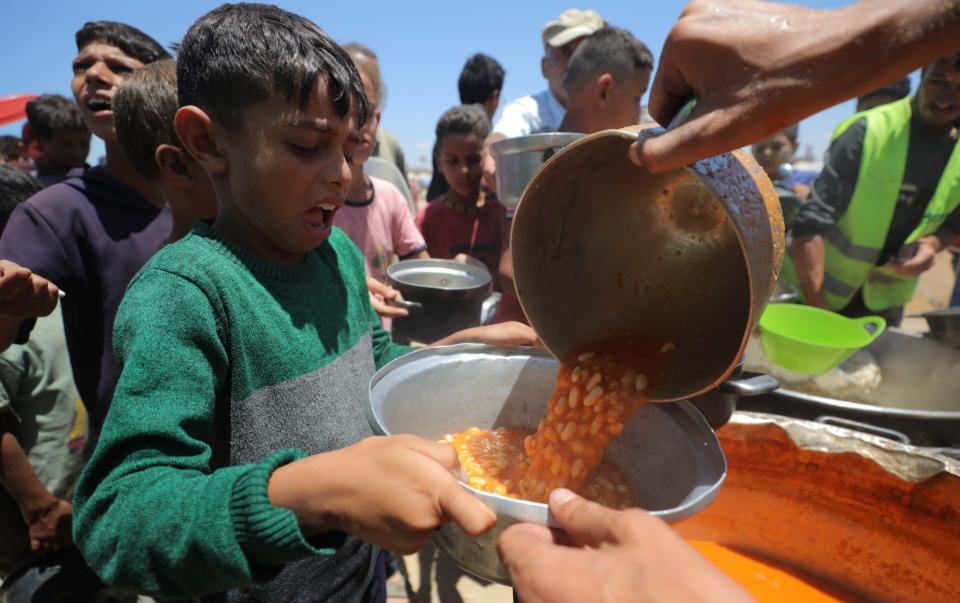 Palestinians, including children, wait in line to receive food distributed by charitable organizations amidst Israeli attacks in Deir Al- Balah, Gaza