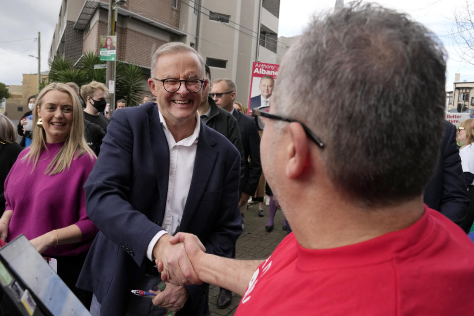Labor Party leader Anthony Albanese, center, shakes hands with a voter he and his partner Jodie Haydon, left, arrive a polling place to cast their ballots in Sydney, Australia, Saturday, May 21, 2022. Australians go to the polls following a six-week election campaign that has focused on pandemic-fueled inflation, climate change and fears of a Chinese military outpost being established less than 1,200 miles off Australia's shore. (AP Photo/Rick Rycroft)