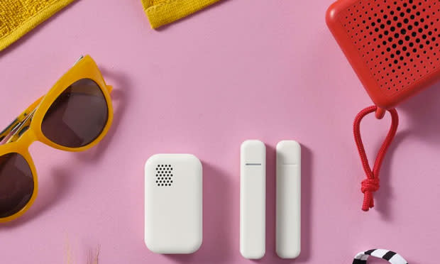 Imagen promocional de los nuevos sensores para el hogar inteligente de IKEA, que son blancos, sobre un fondo rosa junto a un altavoz de plástico rojo y gafas de sol amarillas.