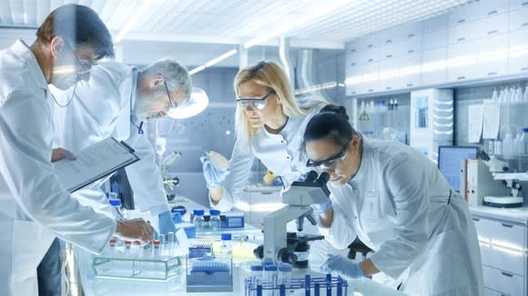 Lab workers with vials and microscope.