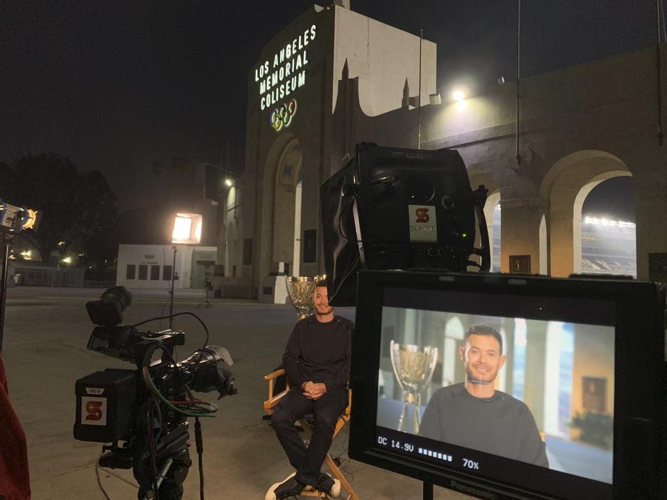 NASCAR driver Kyle Larson is interviewed in front of the Los Angeles Memorial Coliseum, early Tuesday, Nov. 9, 2021, two days after winning the NASCAR Cup Series championship in Avondale, Ariz. Larson toured Los Angeles Memorial Coliseum on Tuesday, the first driver to get an up-close look at what NASCAR plans when it shifts to the season-opening exhibition Busch Clash Feb. 6 on a purpose-built track inside the Coliseum. Larson, as the champion, is the only driver locked into the field so far.(AP Photo/Jenna Fryer)