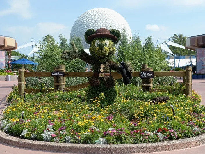 A 3D Mickey Mouse made out of greenery and landscaping standing in front of the Epcot globe.