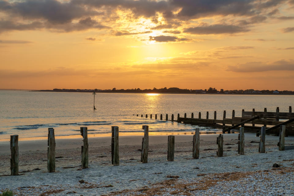 A wooden sea groyne stretches out into a calm sea in the golden light of the setting sun