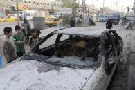 Civilians inspect a damaged vehicle in the aftermath of a Monday car bomb attack in a crowded commercial street in Baghdad's eastern neighborhood of Sadr City, Iraq, Tuesday, April 22, 2014. Suicide bombings and other attacks across Iraq killed and wounded dozens on Monday, officials said, the latest in an uptick in violence as the country counts down to crucial parliamentary elections later this month. (AP Photo/Karim Kadim)