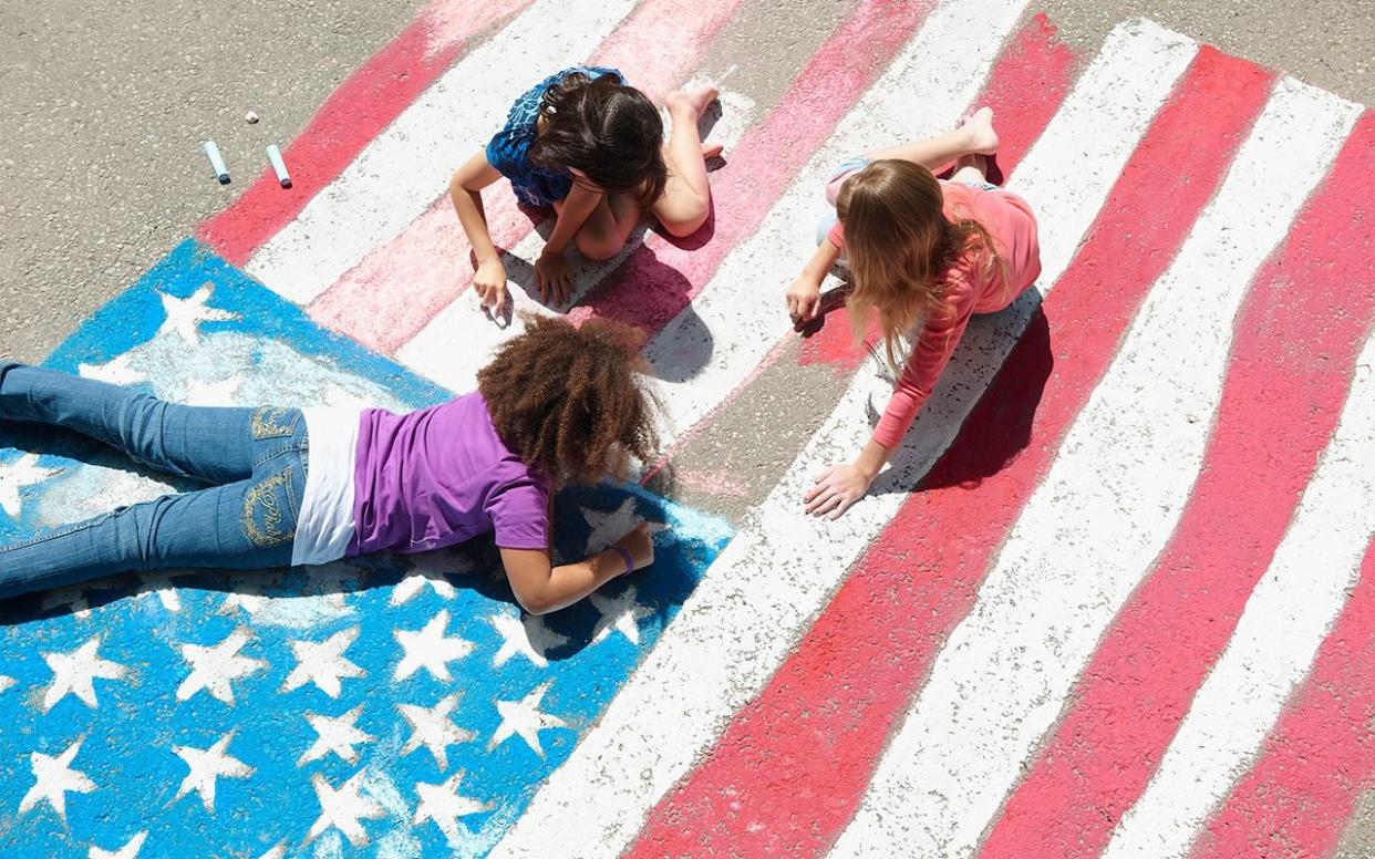 Girls with chalk coloring American flag on sidewalk