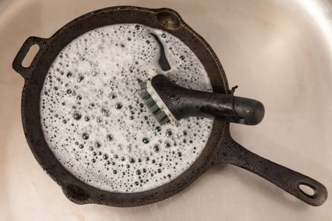 cast iron skillet in sink with soapy water and scrub brush