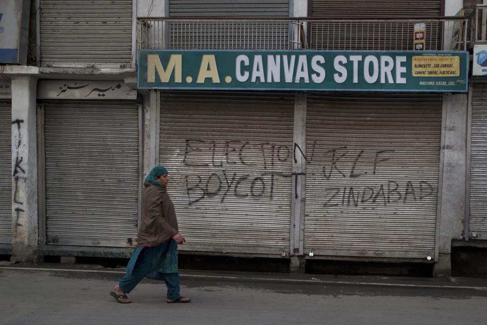 A Kashmiri woman walks past an anti-election graffiti on the shutters of a shop during the second phase of India's general elections, in Srinagar, Indian controlled Kashmir, Thursday, April 18, 2019. Kashmiri separatist leaders who challenge India's sovereignty over the disputed region have called for a boycott of the vote. Most polling stations in Srinagar and Budgam areas of Kashmir looked deserted in the morning with more armed police, paramilitary soldiers and election staff present than voters. (AP Photo/ Dar Yasin)