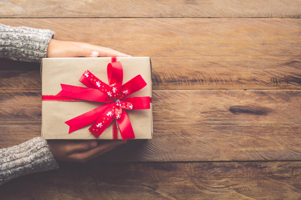 Cropped Hands Of Woman Holding Wrapped Gift On Wooden Table