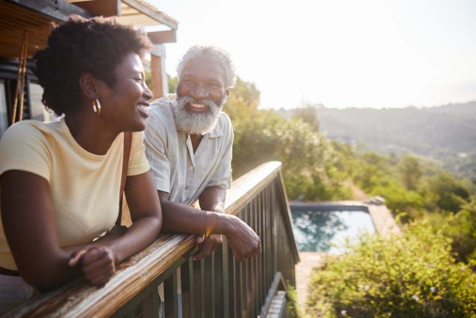 A man and a woman smile while standing on a balcony.