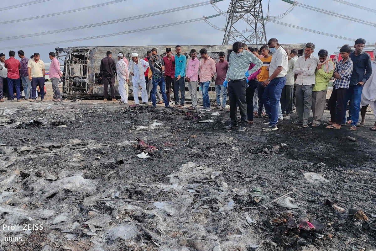 People gather next to the remains of a bus (background) that caught fire along the Samruddhi Expressway (AFP via Getty Images)