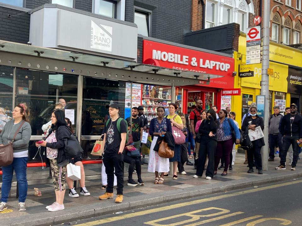 People wait at bus stop outside Clapham Junction (PA)