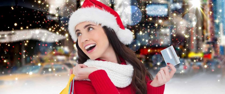 Cheerful woman in santa costume holding shopping bag and credit card against digitally generated sparkling background