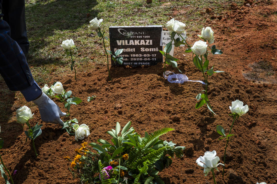 A relative places a rose on the grave of Benedict Somi Vilakasi following his funeral ceremony at the Nasrec Memorial Park outside Johannesburg Thursday, April 16, 2020. Vilakasi, a Soweto coffee shop manager, died of Covid-19 infection in a Johannesburg hospital Sunday April 12 2020. South Africa is under a strict five-week lockdown in a effort to fight the Coronavirus pandemic. (AP Photo/Jerome Delay)