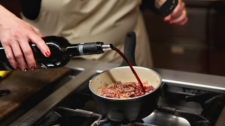 Chef pouring wine into pasta sauce