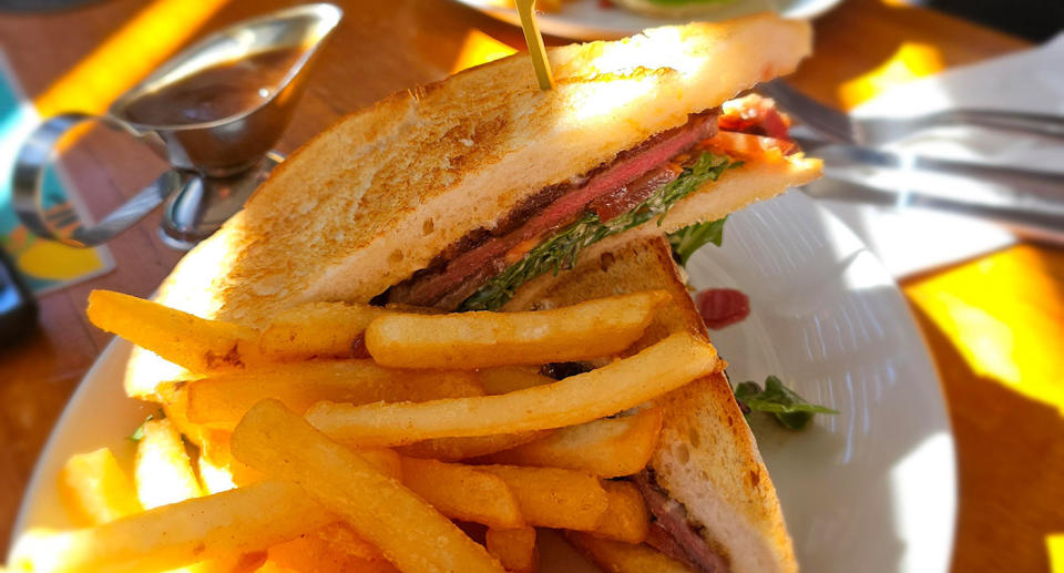 A steak sandwich on a plate with hot chips