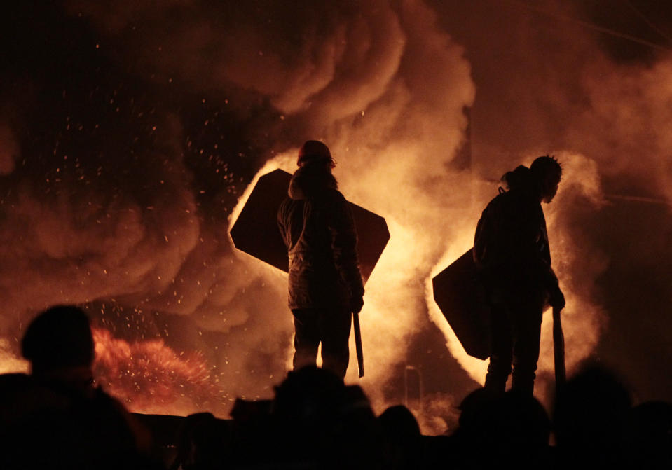 Manifestantes armados con palos y barras de hierro se preparan para un posible choque con la policía en el centro de Kiev, Ucrania, el sábado 25 de enero de 2014. El fuego y el humo provienen deben a neumáticos incendiados en barricadas que levantaron los inconformes. (AP Foto/Sergei Chuzavkov)
