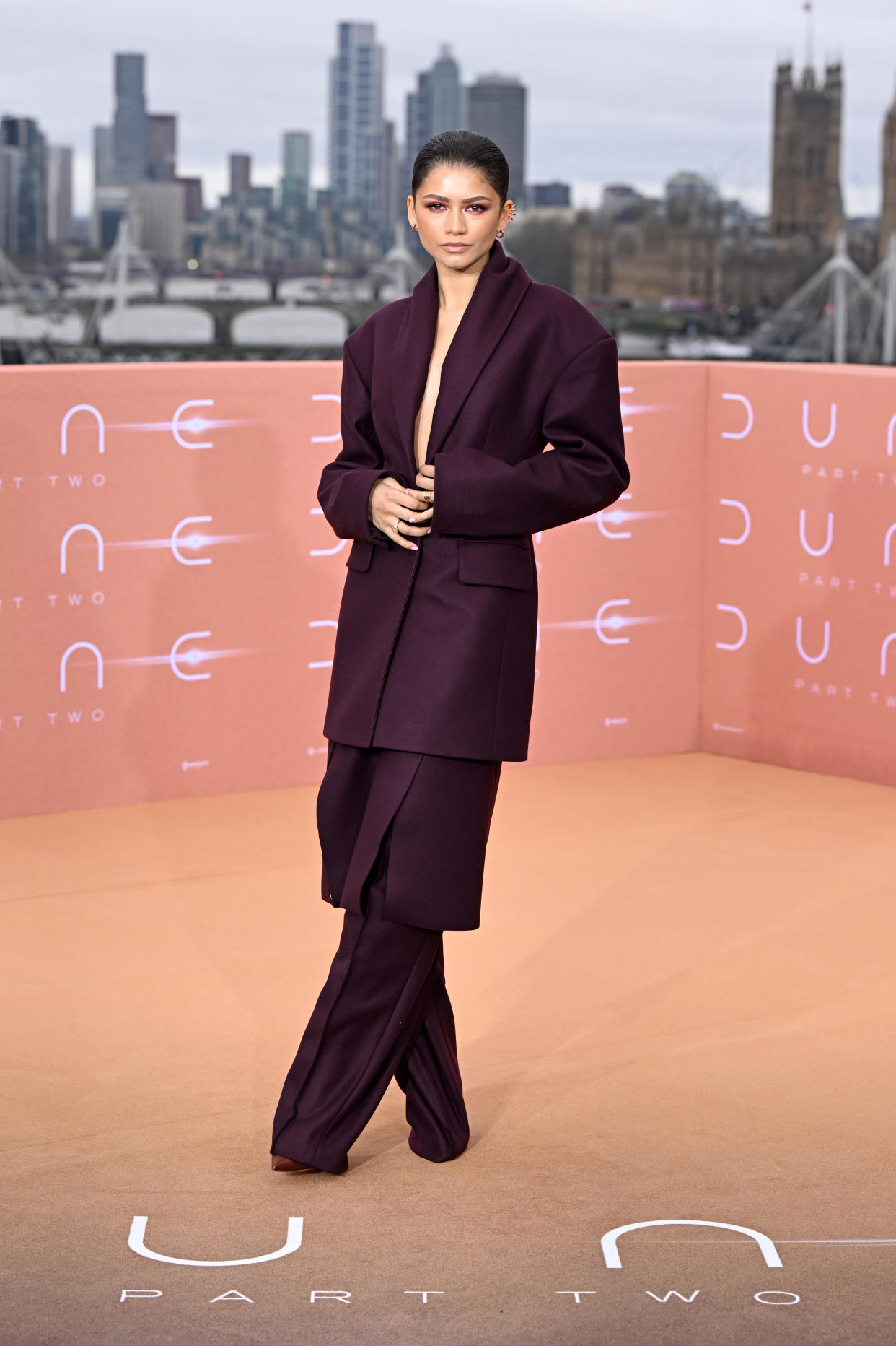 The actress wears a long jacket, pants and a skirt overlay as she poses on a rooftop.