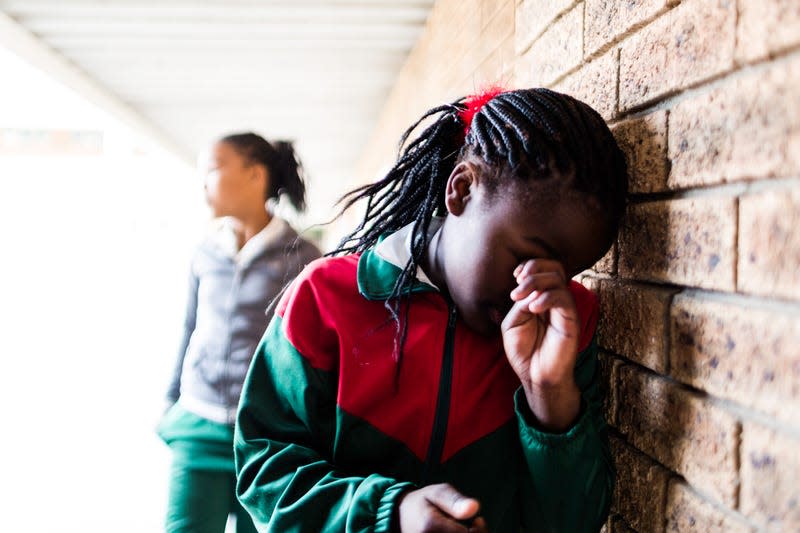 A stock photo of a school girl stands leaning against a wall crying, she is being bullied by other girls at her school. - Photo: GeorgiaCourt (iStock by Getty Images)