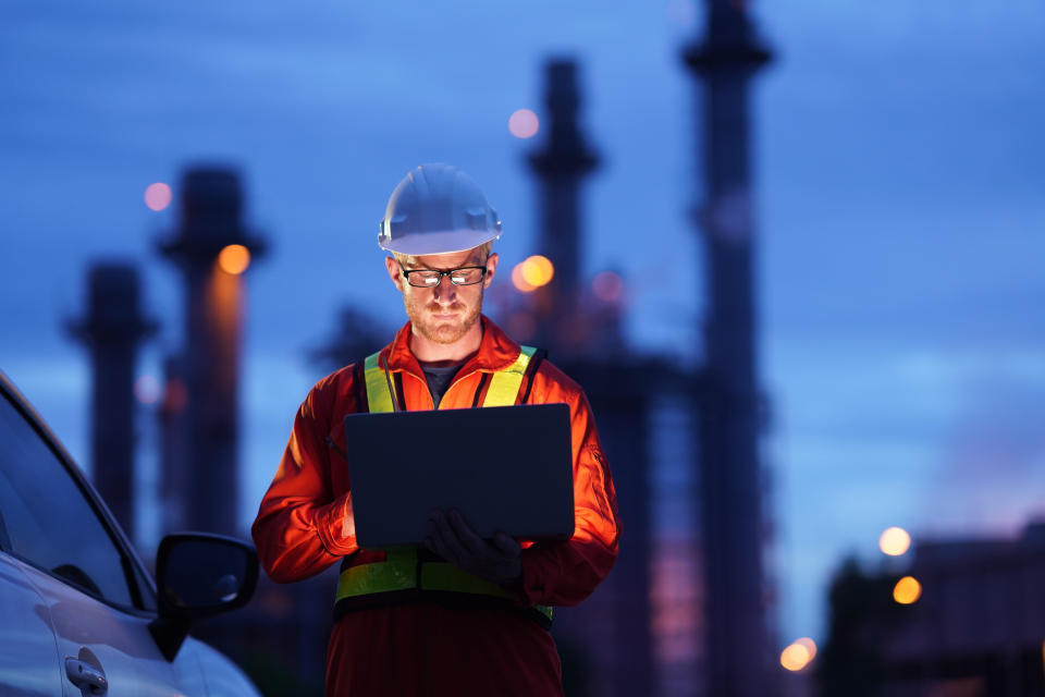 Engineer using laptop working while standing over Natural gas power Plant at construction site in evening twilling