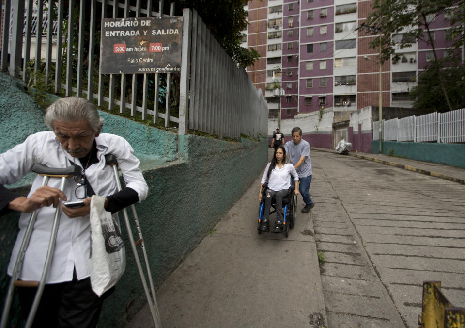 In this Dec. 17, 2018 photo, neighbor Dixon Rosales helps dancer Iraly Yanez negotiate her wheelchair on a downhill path, in Caracas, Venezuela. A stray bullet crushed Yanez's aspirations of becoming a professional dancer eight years ago as it ruptured two of her vertebrae and left her paraplegic. (AP Photo/Fernando Llano)