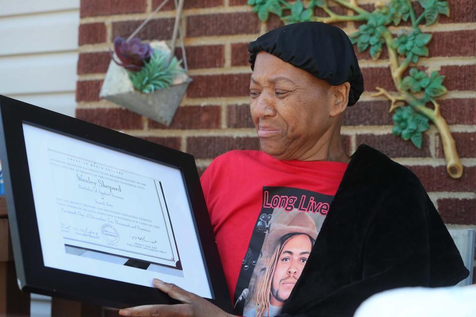 Rebecca Shepard, who is battling cancer, becomes tearful as she looks at the media arts diploma of her late son Wesley, who is pictured on the shirt she is wearing.