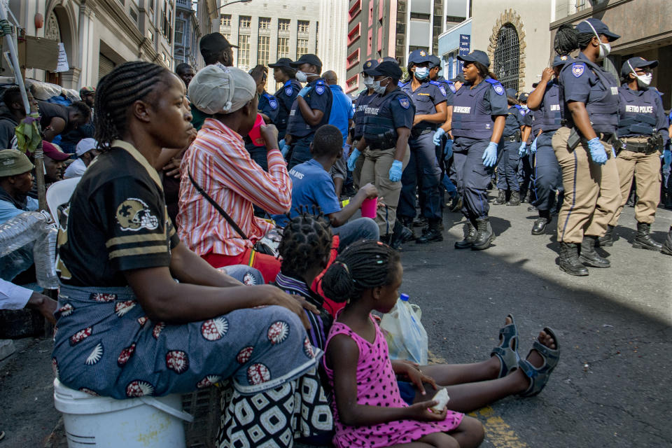 People sit with their belongings, outside the Central Methodist Mission Church in Cape Town, South Africa, Sunday, March 1, 2020 as city officials and police move in to evict them. Hundreds of migrants have been removed from central Cape Town by South African authorities following a months-long stand-off. The migrants removed on Sunday had demanded to be relocated to other countries claiming they had been threatened by xenophobic violence last year. (AP Photo)