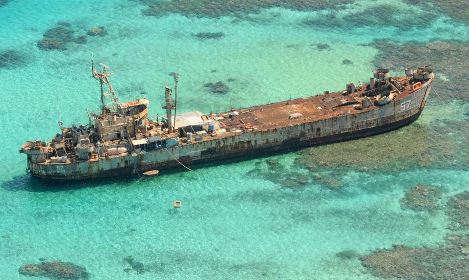 A photo of a rusted boat sitting in clear blue water.